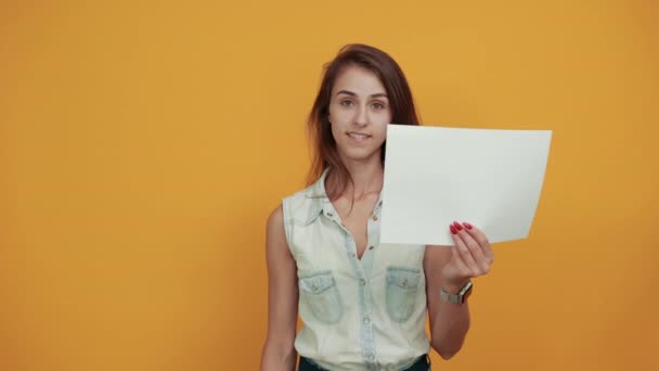 Mooie vrouw in blauw denim shirt houdt wit papier, houdt vuist omhoog, glimlacht — Stockvideo