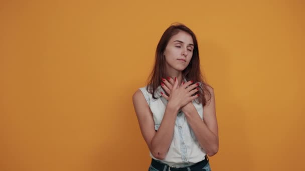 Charmante jonge vrouw die handen op de borst houdt, er kalm uitziet met gesloten ogen — Stockvideo