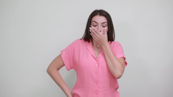 Vonzó fiatal nő rózsaszín ingben tartja a kezét a száján, ijedtnek tűnik. — Stock videók