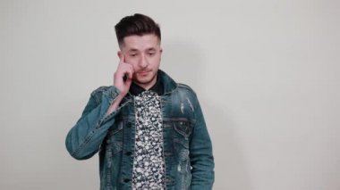 Moda gömlekli genç yakışıklı adam ellerini yanaklarından ayırmıyor, doğrudan bakıyor.