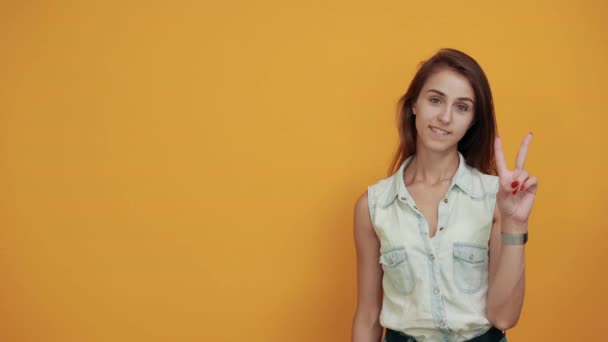 Attractive young woman in blue denim shirt doing victory gesture, smiling — Stock Video