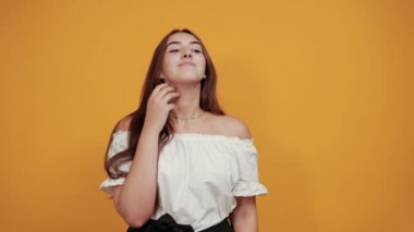 Çekici genç bir kadın. Parmağını yanağında tutuyor. Turuncu duvarda güzel görünüyor.