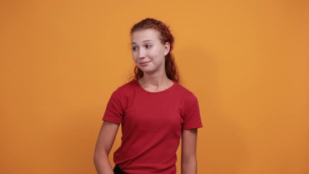 Jovencita sonriente en camisa roja mostrando espacio a un lado, manteniendo la mano en la cintura — Vídeos de Stock