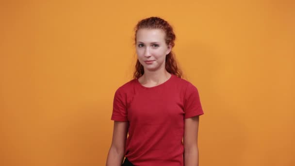 Bonita jovencita con camisa roja sonriendo, señalando directamente — Vídeos de Stock