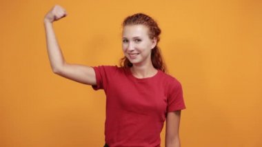 Kırmızı gömlekli güçlü genç kadın kameraya kaslarını gösteriyor, mutlu görünüyor.