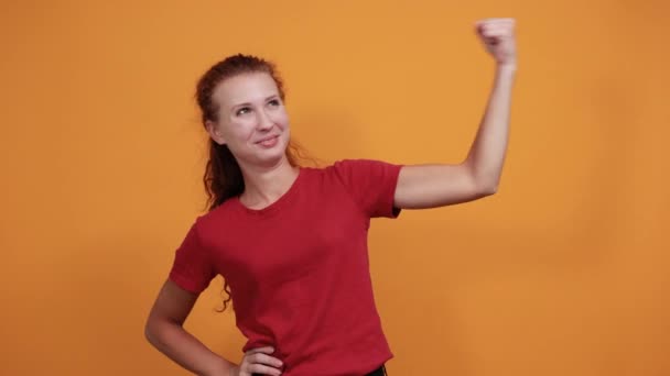 Bella giovane signora in camicia rossa che mostra i muscoli, cercando felice — Video Stock
