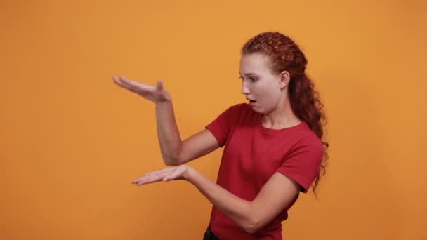 Hezká mladá dáma v červené košili ukazuje prostor mezi rukama, vypadá zmateně — Stock video