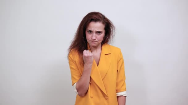 Vonzó nő sárga kabátban dühösnek tűnik, ökölbe szorítja a kezét, fenyeget.. — Stock videók