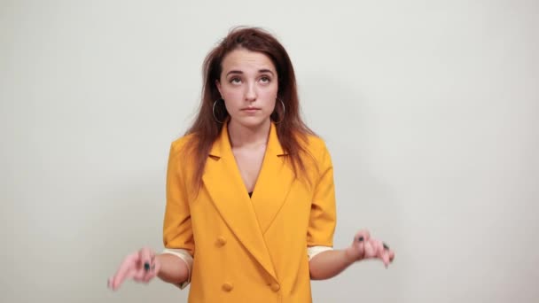 Mujer atractiva en chaqueta amarilla manteniendo el dedo cruzado, mirando confundido — Vídeos de Stock