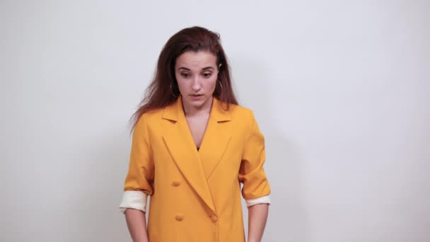 Потрясенная молодая женщина в желтой куртке, держащая руку на голове, выглядящая смущенной — стоковое видео
