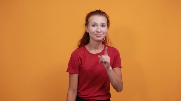 Bonita joven con camisa roja invitar a alguien, manteniendo el dedo en la barbilla — Vídeos de Stock