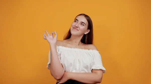 Cheerful young woman doing victory gesture, smiling isolated on orange wall