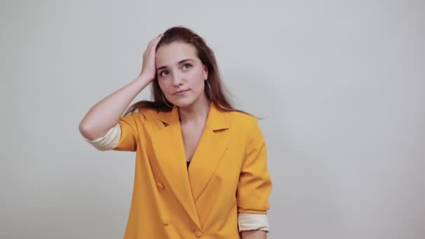 Jolie jeune femme en veste jaune gardant la main sur la tête sur le mur gris — Video