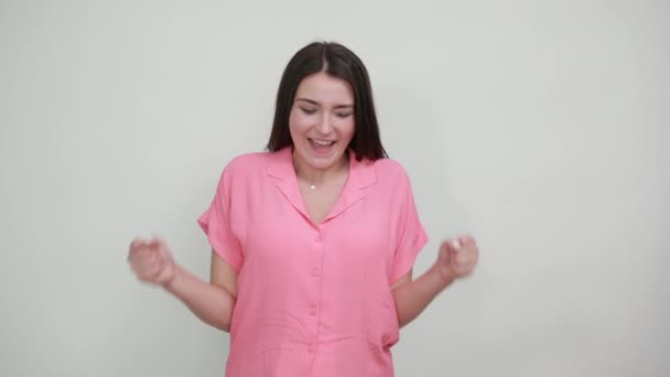 Aantrekkelijke jonge vrouw houden vuisten omhoog, glimlachen geïsoleerd op grijze muur — Stockvideo
