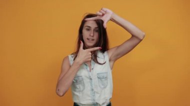 Neşeli beyaz kadın parmaklarıyla çerçeve yapıyor, mutlu görünüyor.