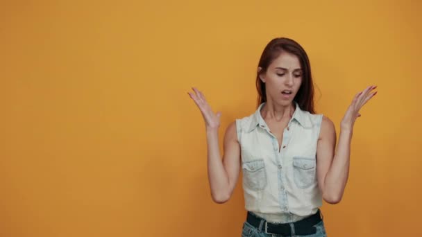 Kaukázusi fiatal nő kék farmer ing megdöbbent, széttárja a kezét a narancssárga fal — Stock videók