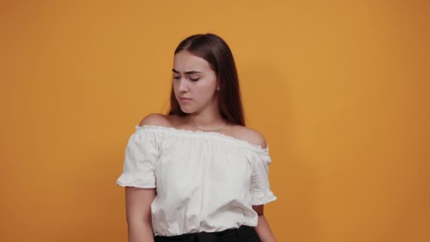 Розчарована молода жінка спрямовує великий палець вниз ізольовано на помаранчевій стіні — стокове відео
