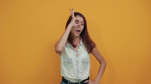 Attractive young woman in blue denim shirt showing okay gesture near eyes — Stock Video