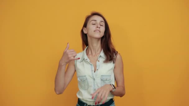 Досить біла молода жінка в синій джинсовій сорочці робить жест телефону — стокове відео