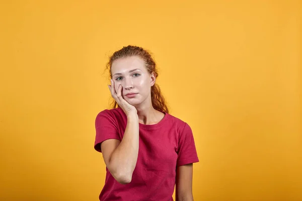 Aborrecido jovem senhora em camisa vermelha mantendo a mão no queixo, pensando sobre a questão — Fotografia de Stock