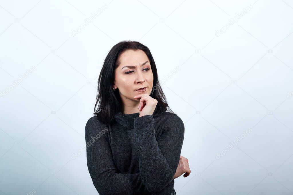 Serious caucasian young woman keeping hand on chin, thinking about something