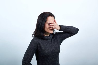 Çekici, beyaz, genç bir kadın. Elleriyle gözlerini kapatmış, gülümsüyor.