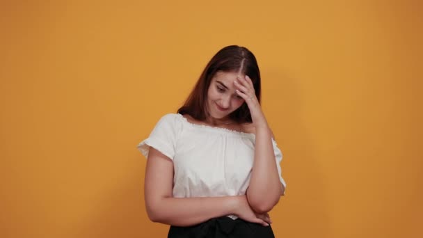 Mulher triste mantendo a mão na cabeça, dor de cabeça, cabelo fluttering isolado na parede laranja — Vídeo de Stock