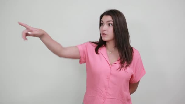 Shocked young woman pointing aside, keeping hand behind back — Stock Video