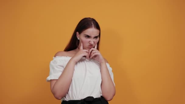 Mujer joven seria manteniendo las manos en la cabeza, mirando sorprendido en la pared naranja — Vídeos de Stock