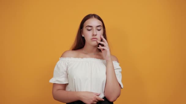 Unhappy young woman keeping finger on near eyes, crying on orange wall — Stock Video