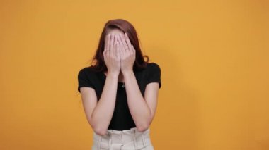 Siyah gömlekli kadın elleriyle yüzünü kapatıyor, parmaklarından bakıyor.