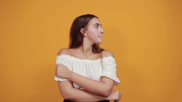 Attractive young woman keeping finger on mouth, looking pretty on orange wall. — Stock Video