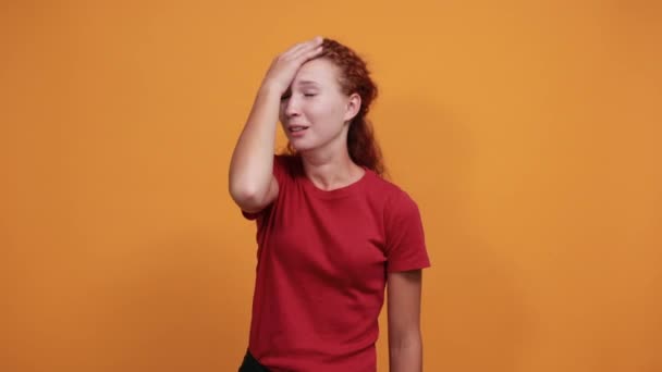 Aantrekkelijke dame in rood shirt houdt hand op hoofd, glimlacht, ziet er gelukkig uit — Stockvideo