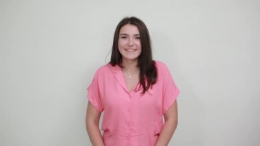 Neşeli genç bir kadın parmaklarını yanaklarından ayırmıyor, gülümsüyor, güzel görünüyor.