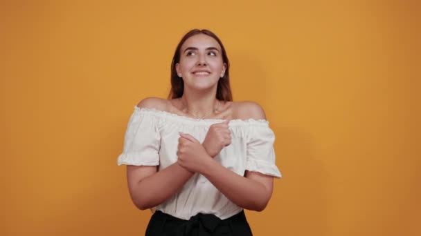 Glada ung kvinna tittar upp, hålla handen korsad på orange vägg — Stockvideo
