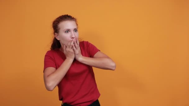 Wystraszona młoda dama w czerwonej koszuli przykrywająca usta dłonią, wyglądająca na przerażoną — Wideo stockowe