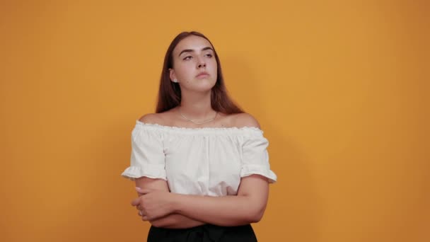 Jolie jeune femme gardant la main sur le menton, en pensant à la question sur le mur orange — Video