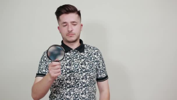 Handsome man in fashion shirt holding a magnifying glass, looking on it — Stock Video