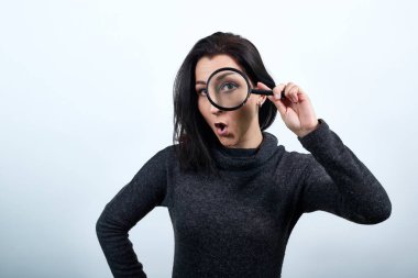 Şok olmuş genç bir kadın, büyüteçleri gözünün yanında tutuyor, el ele tutuşuyor.