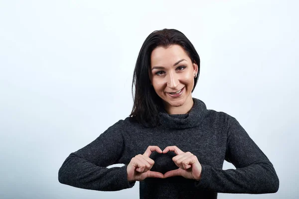 Attraktive kaukasische junge Frau zeigt Herzform und lächelt. — Stockfoto