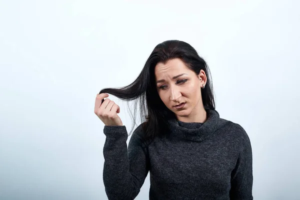 Disappointed woman holding hair with hands, corrects haircut, looking confused