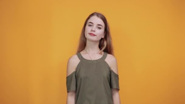 Милая молодая женщина в хаки оранжевой рубашке держит палец на щеке, улыбаясь — стоковое видео