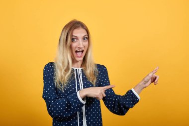 Şok olmuş genç bir bayan turuncu duvarın üstünden ağzı açık bir şekilde gösteriyor.