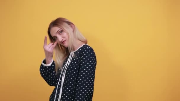 Мода чарівна молода леді робить рок-символ жест над ізольованою помаранчевою стіною — стокове відео