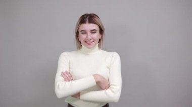 Gri duvarda el ele tutuşmuş gülümseyen genç bir kadın.