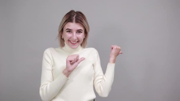 Mujer señalando a un lado, manteniendo el pulgar hacia arriba, sonriendo para presentar un producto — Vídeo de stock