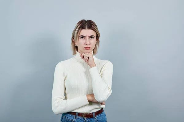 Porträtt av förvirrad ung kvinna tittar åt sidan och ckeeping finger på hakan — Stockfoto