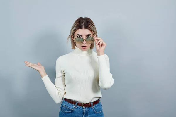 Spännande ung flicka i vita kläder håller solglasögon ser rädd — Stockfoto