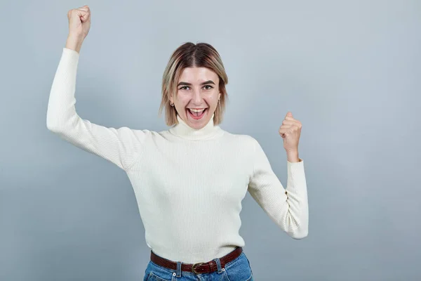 Ung kvinna står gör vinnaren gest med armarna upp, ler för framgång. — Stockfoto