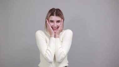 Sıradan süveter giyen çekici genç bir kadın. Elleri yanaklarında, mutlu görünüyor.